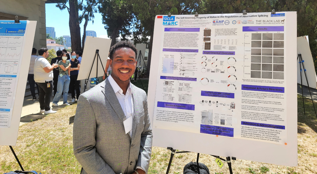 Student standing in front of research presentation poster at a poster session event.