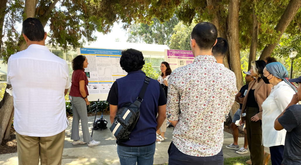 Student standing in front of research poster with crowd of people watching her discuss research with her mentor.